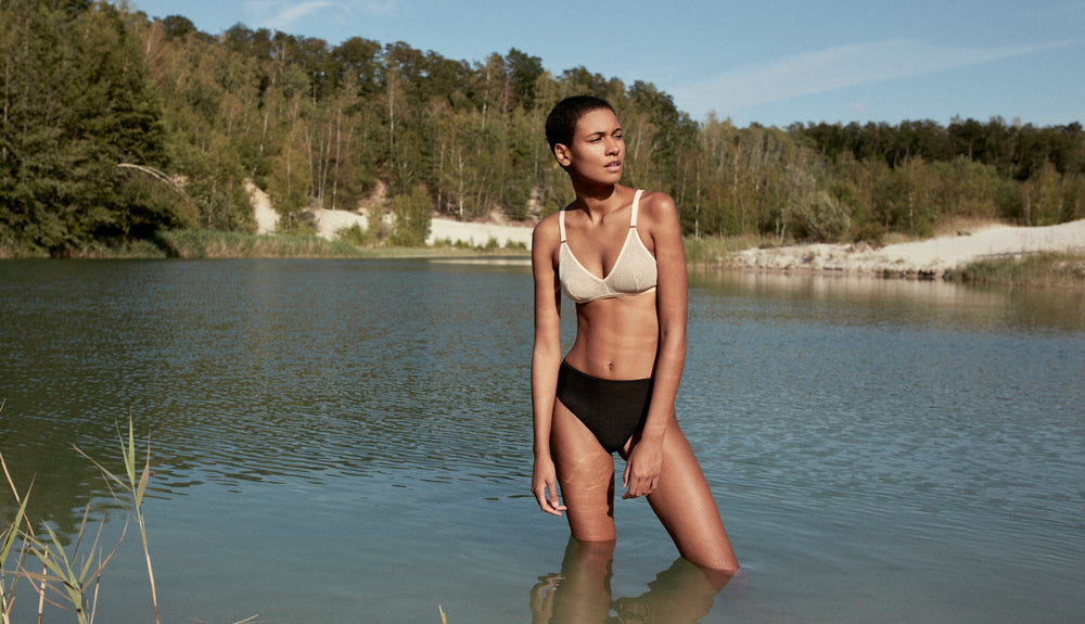 Femme les jambes dans l'eau en plein nature portant un ensemble de slow lingerie soutien-gorge et tanga haut tulle