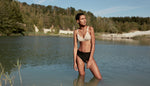 Femme les jambes dans l'eau en plein nature portant un ensemble de slow lingerie soutien-gorge et tanga haut tulle